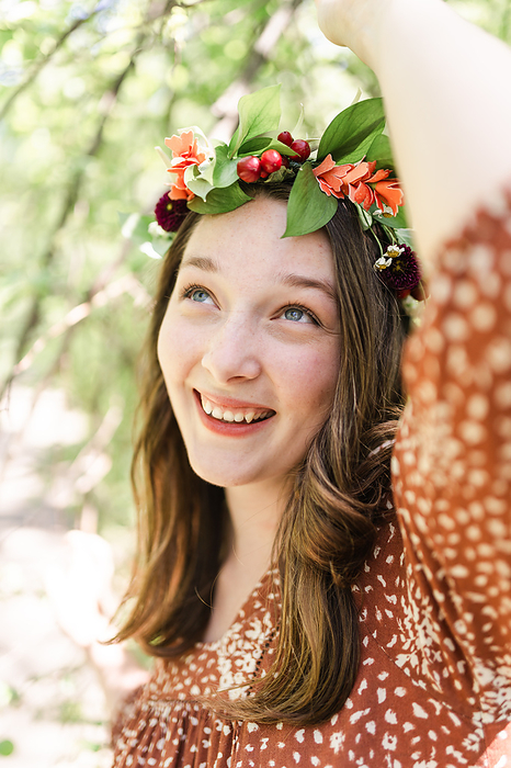 A woman with a flower crown grabbing a tree branch, by Cavan Images / Jade Boyd