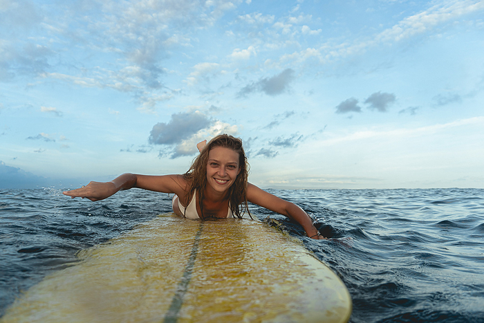 Happy woman on surfboard in sea, Bali., by Cavan Images / Yuliya Kirayonak