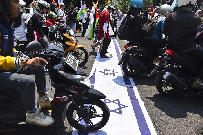 Thousands of people at Pro Palestinian Demonstration in West Java Indonesia Indonesian Muslims place a poster picturing the Israeli flag on a street to be run over by passing vehicles as they gather for a pro Palestinian demonstration in Bandung, West Java,Indonesia on October 21, 2023. Thousands of people attend the demonstration to condemn against the genocide of the government of Israel and express solidarity with the Palestinian people.