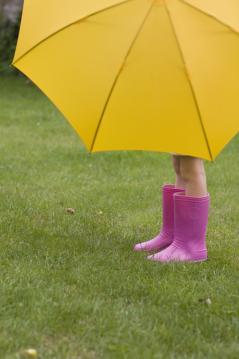 Young girl in pink boots under yellow umbrella, by Ableimages