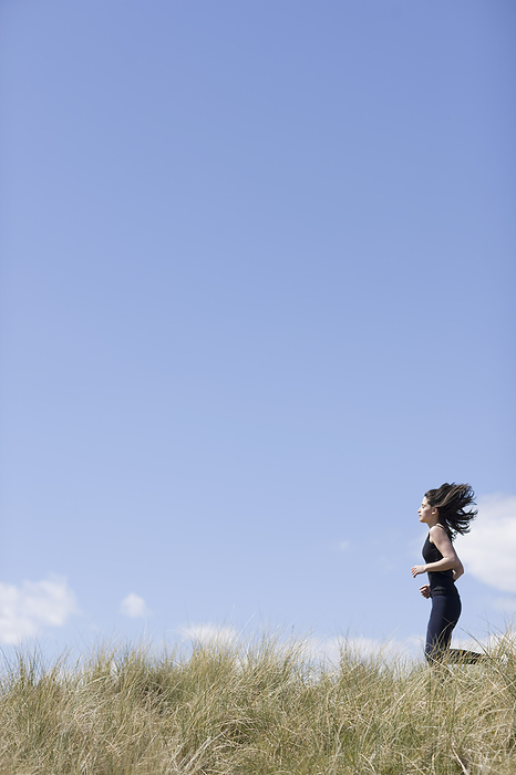 Young woman running through sand dunes, by Ableimages