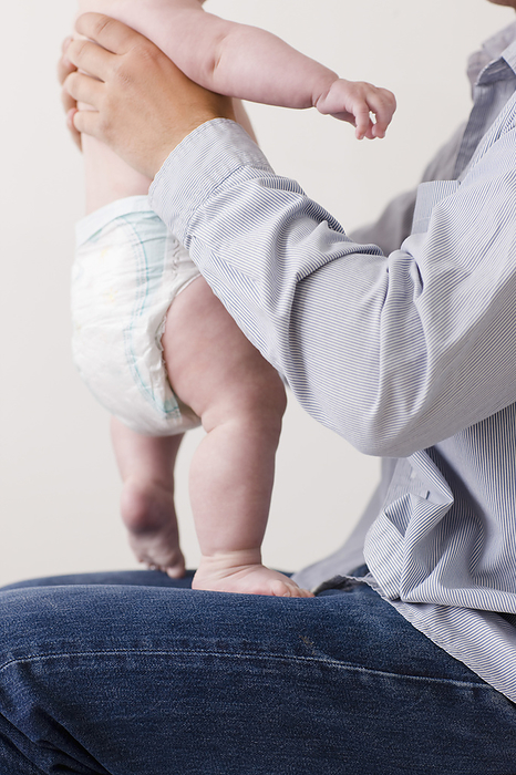 Man sitting with newborn baby standing on his lap, by Ableimages