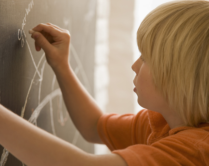 Young boy writing on a blackboard, by Jutta Klee