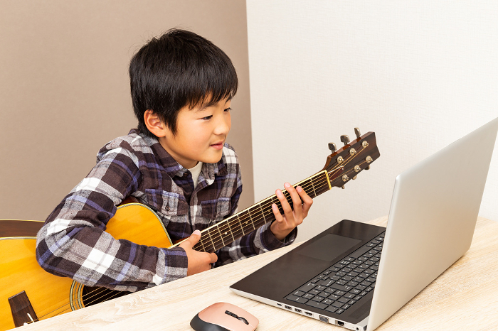 Boy playing guitar while looking at computer