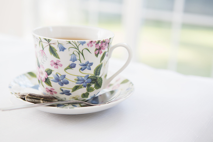 Cup of tea in pretty floral cup with saucer and used tea bag, studio shot, by Amy Whitt / Design Pics