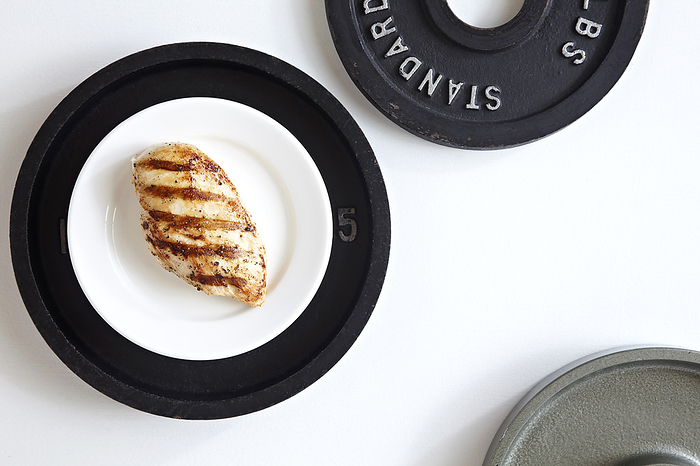 Grilled Chicken breast on a white plate on top of a weight plate, studio shot on white background, by Jodi Pudge / Design Pics