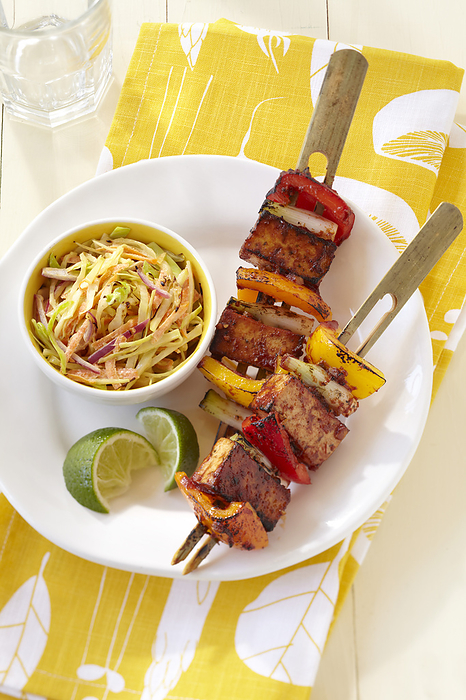 Grilled tofu and bell peppers on bamboo skewers with side dish of slaw and lime wedges on a yellow patterned napkin, by Jodi Pudge / Design Pics