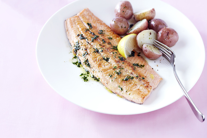 Fillet of trout with lemon herb butter and baby potatoes on a pink background, by Jodi Pudge / Design Pics