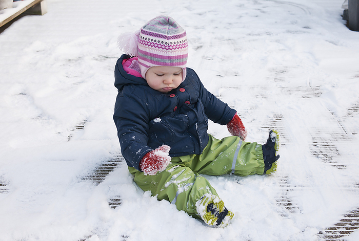 Baby Girl wearing Snow Suit sitting on Ground in Snow, by I. Jonsson / Design Pics