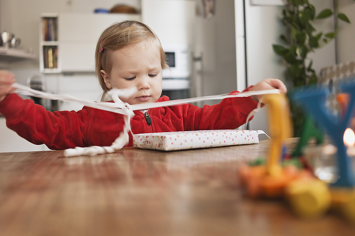 Little Girl Sitting at Table Unwrapping Gift, by I. Jonsson / Design Pics