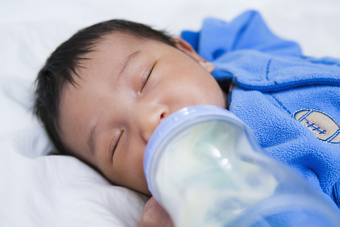 Close-up of two week old Asian baby girl sleeping while drinking from bottle, studio shot, by Mui Chao / Design Pics