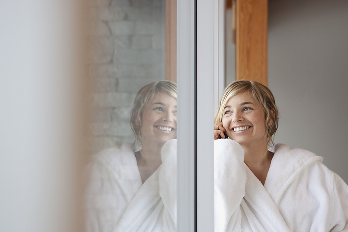 Woman in Bathrobe Talking on Cell Phone and Looking Out the Window, by Noel Hendrickson / Design Pics
