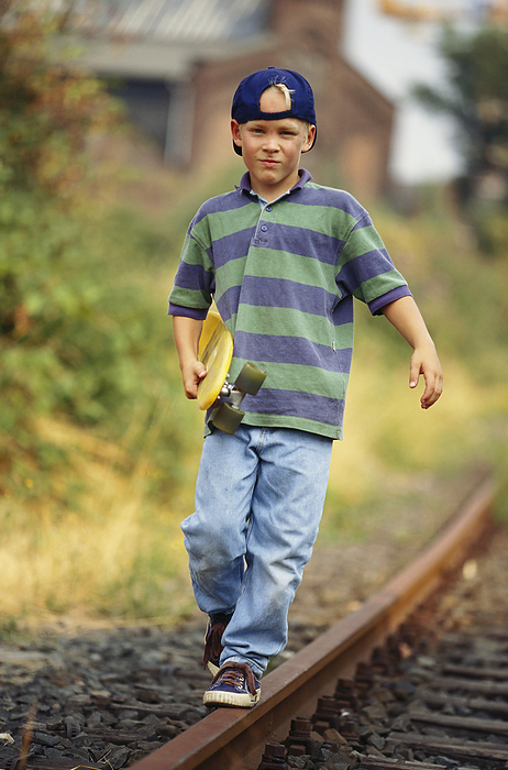 Boy With Skateboard Walking Along Train Tracks, by Norbert Schäfer / Design Pics