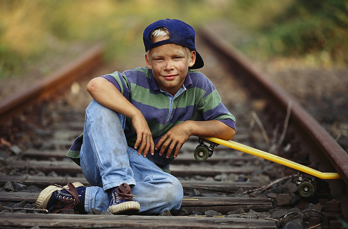Boy With Skateboard Sitting On Train Tracks, by Norbert Schäfer / Design Pics