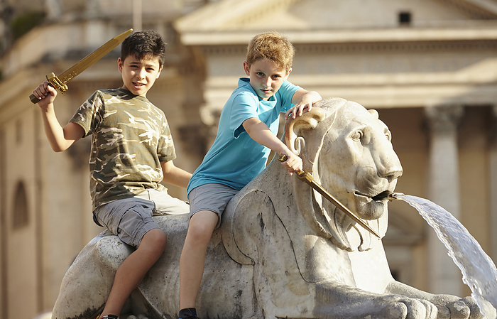 Portrait of two children on lion statue at Fontana dell'Obelisco, Piazza del Popolo (People's Square) on summer vacation, Rome, Lazio, Italy, by Peter Reali / Design Pics