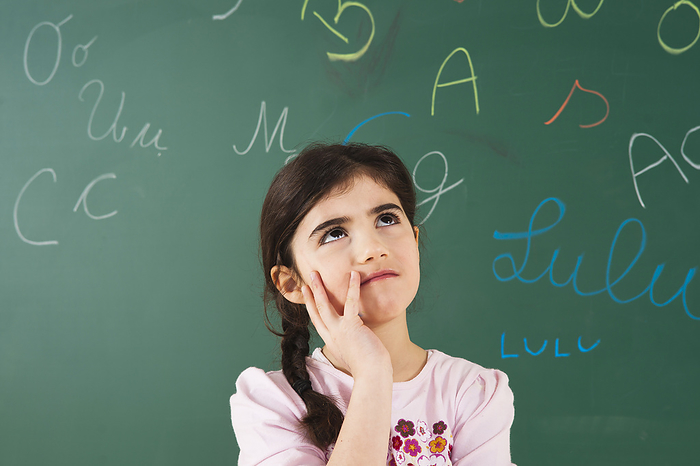 Girl Looking up and Thinking in front of Chalkboard in Classroom, by Uwe Umstätter / Design Pics