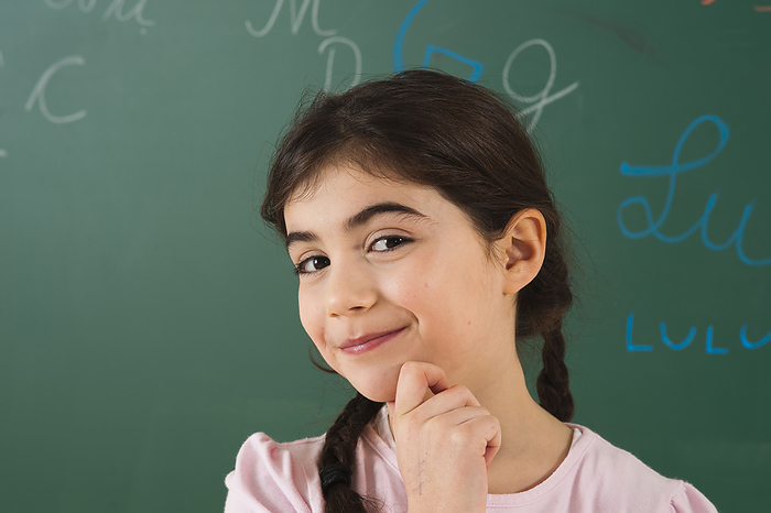 Girl with Hand on Chin in Front of Chalkboard in Classroom, by Uwe Umstätter / Design Pics