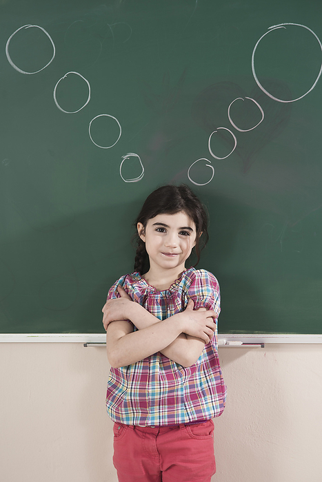 Girl in front of Chalkboard with Thought Bubbles in Classroom, by Uwe Umstätter / Design Pics