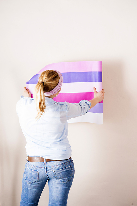 Studio Shot of Young Woman Holding Wallpaper up to Wall, by Uwe Umstätter / Design Pics
