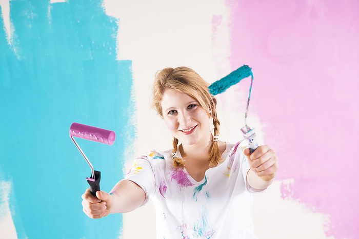 Studio Shot of Young Woman Holding Paint Rollers, Deciding Between Paint Colours, by Uwe Umstätter / Design Pics