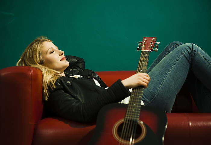 Woman Lying on Sofa and Holding Acoustic Guitar, by Uwe Umstätter / Design Pics