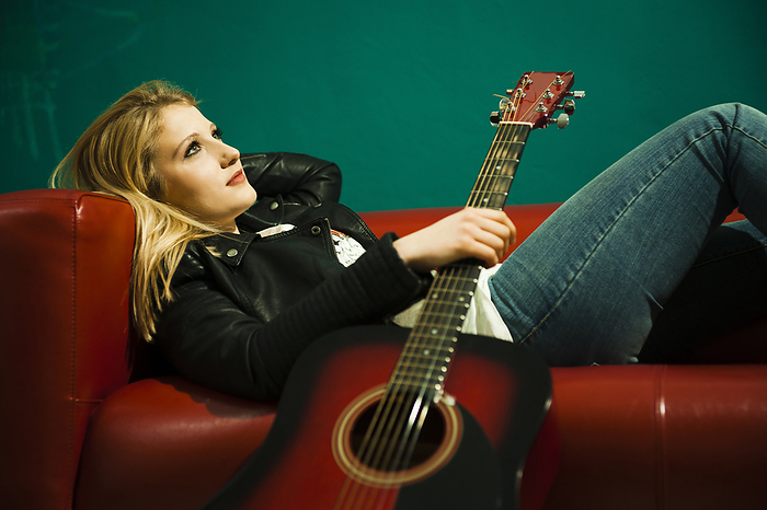 Woman Lying on Sofa and Holding Acoustic Guitar, by Uwe Umstätter / Design Pics