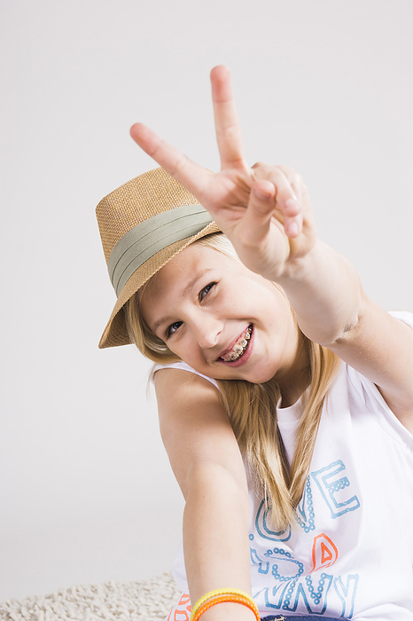 Portrait of Girl wearing Hat and making Peace Sign Gesture in Studio, by Uwe Umstätter / Design Pics