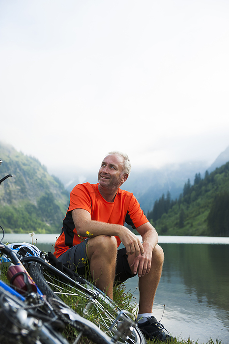 Mature Man Sitting by Lake with Mountain Bike, Vilsalpsee, Tannheim Valley, Tyrol, Austria, by Uwe Umstätter / Design Pics