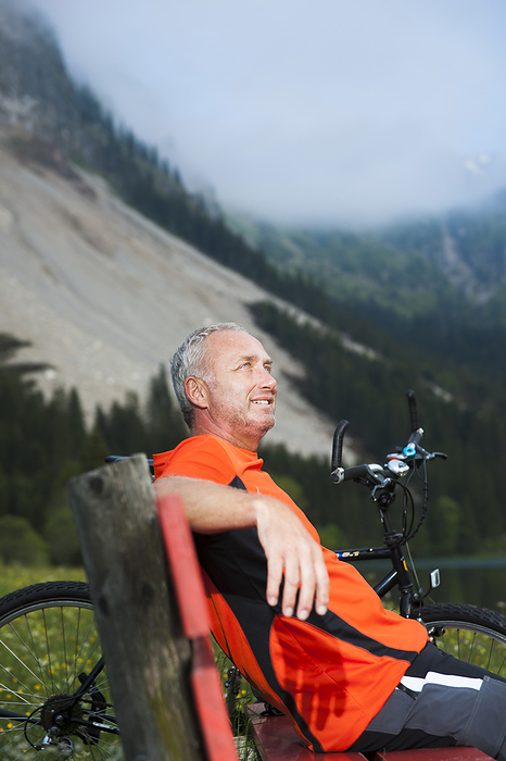 Mature Man on Bench by Lake with Mountain Bike, Vilsalpsee, Tannheim Valley, Tyrol, Austria, by Uwe Umstätter / Design Pics