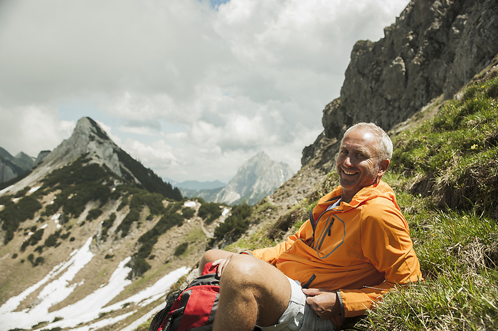 Portrait of mature man sitting on grass, hiking in mountains, Tannheim Valley, Austria, by Uwe Umstätter / Design Pics
