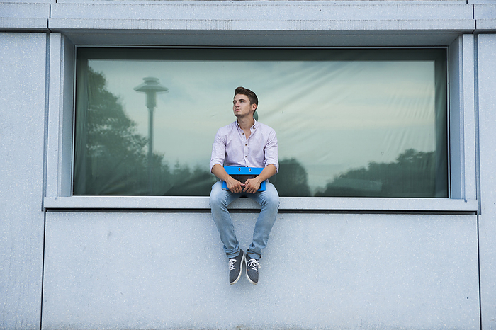 Young man sitting on ledge outdoors, Germany, by Uwe Umstätter / Design Pics