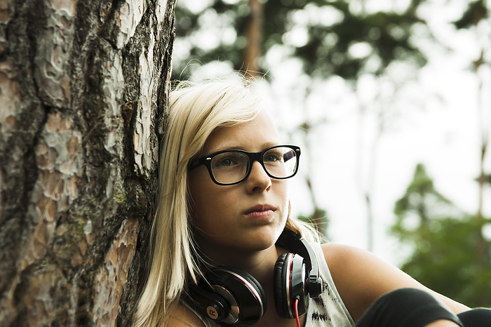 Close-up portrait of girl wearing eyeglasses, sitting next to tree in park, with headphones around neck, Germany, by Uwe Umstätter / Design Pics