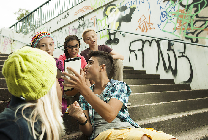 Group of children sitting on stairs outdoors, using tablet computers and smartphones, Germany, by Uwe Umstätter / Design Pics