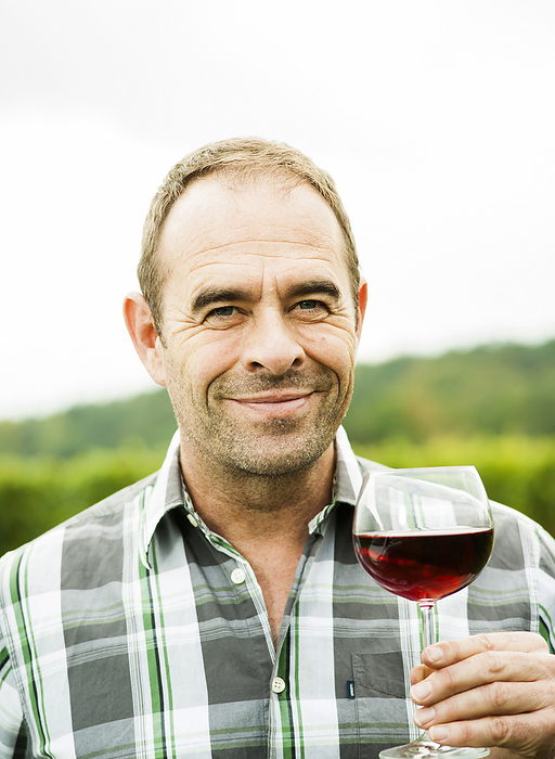 Close-up portrait of vintner standing in vineyard, holding glass of wine, smiling and looking at camera, Rhineland-Palatinate, Germany, by Uwe Umstätter / Design Pics