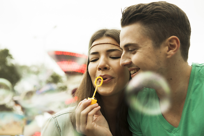 Close-up portrait of young couple blowing bubbles at amusement park, GermanyYoung, by Uwe Umstätter / Design Pics