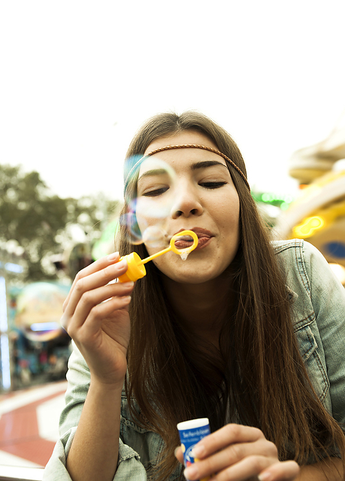 Close-up portrait of teenage girl blowing bubbles at amusement park, Germany, by Uwe Umstätter / Design Pics