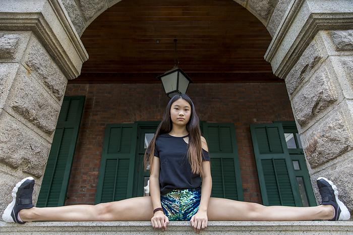 Preteen girl in a splits position on a ledge under an archway; Hong Kong, China, by Ian Taylor / Design Pics