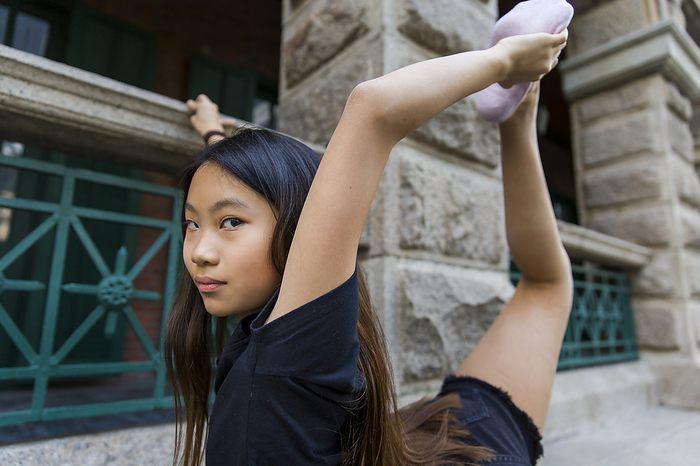 Preteen girl stretches with dance shoes; Hong Kong, China, by Ian Taylor / Design Pics