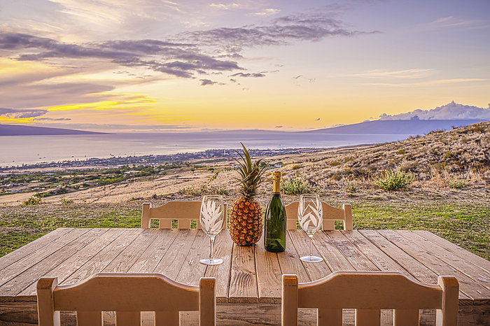 Maui, Hawaii Pineapple, bottle of wine and two wine glasses sitting on a wooden table with chairs on a hilltop overlooking Launiupoko and the Pacific Ocean at sunset with the Island of Lanai in the distance  Maui, Hawaii, United States of America, by Living Moments Media   Design Pics