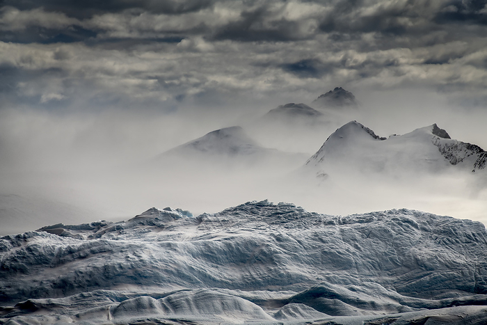 Antarctica Iceberg in the foreground acts like a stage for wind whipped snow blowing past mountains lining Iceberg Alley on the way to the western Antarctica Peninsula  Antarctica, by Karen Kasmauski   Design Pics