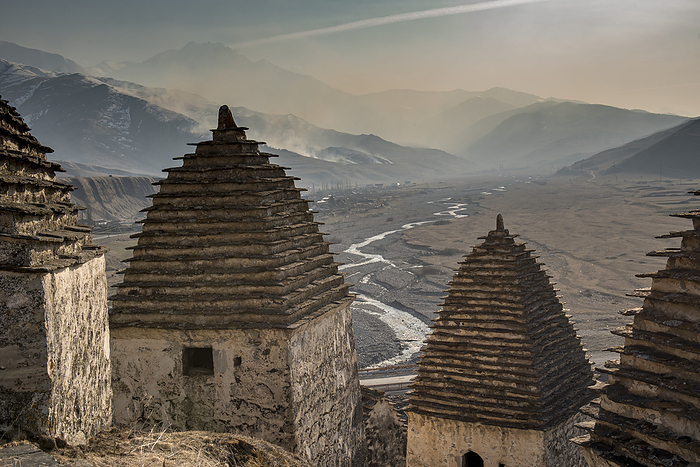 Russia Abandoned village with traditional conical roofed shelters on the mountainside in Ingushetia, looking down at the hazy mountainous landscape below  Republic of Ingushetia, Russia, by Christopher Roche   Design Pics
