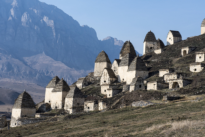 Russia Abandoned village with traditional conical roofed shelters on the mountainside in Ingushetia with jagged mountain ridges in the background  Republic of Ingushetia, Russia, by Christopher Roche   Design Pics