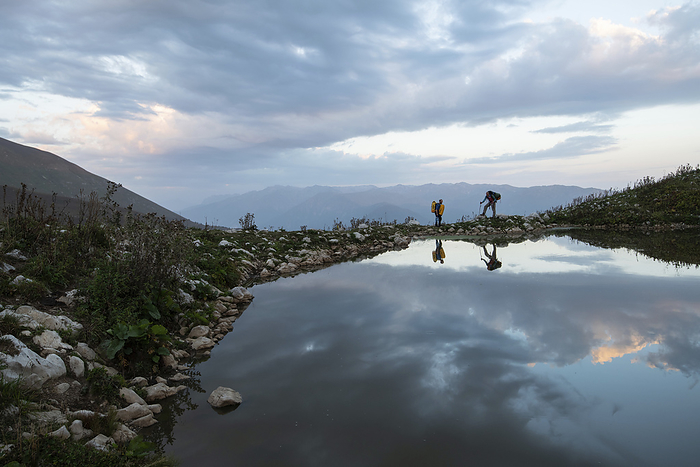 Adventure exploration expedition as two explorers stop for a rest next to a small lake on their way to a base camp close to Veryovkina, cave entrance high in the Caucasus Mountains; Gagra, Caucasus Mountains, Abkhazia, by Robbie Shone / Design Pics