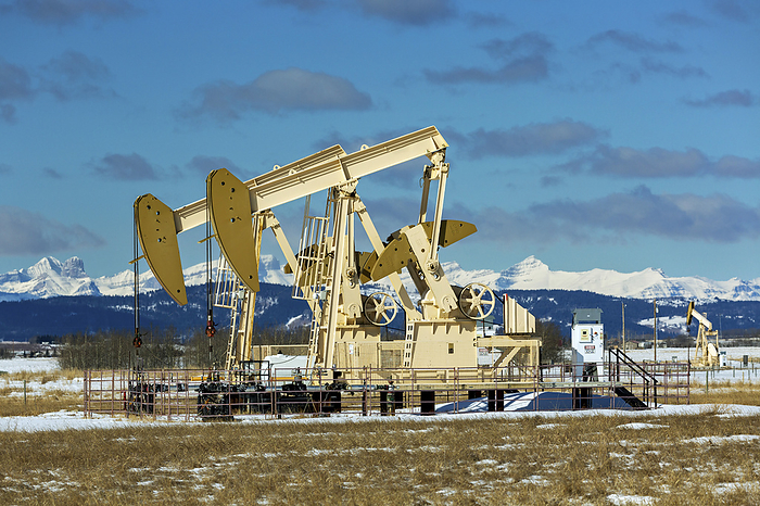Canada Pumpjacks  in a snow covered field with snow covered Rocky Mountains in the background with blue sky and clouds, West of Airdrie  Alberta, Canada, by Michael Interisano   Design Pics