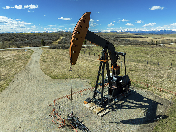 Close up aerial view of a pump jack with blue sky and mountains in the background, North of Longview, Alberta; Alberta, Canada, by Michael Interisano / Design Pics