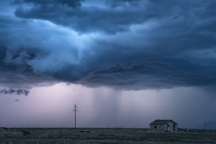 Lightning illuminates the storm clouds above an old cabin; Alberta, Canada, by Robert Postma / Design Pics