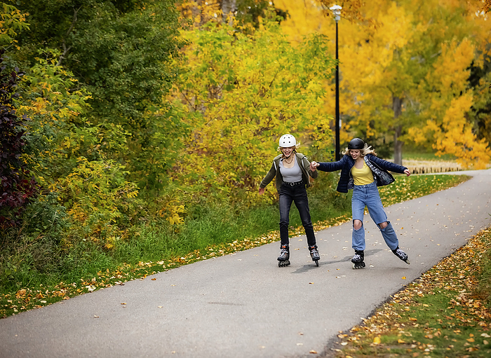 Two teenagers rollerblading together in a city park during a warm fall afternoon; St. Albert, Alberta, Canada, by LJM Photo / Design Pics