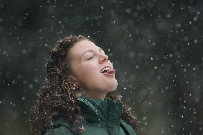 Young woman catching snowflakes with her tongue while standing in a snowfall; Lincoln, Nebraska, United States of America, by Joel Sartore Photography / Design Pics