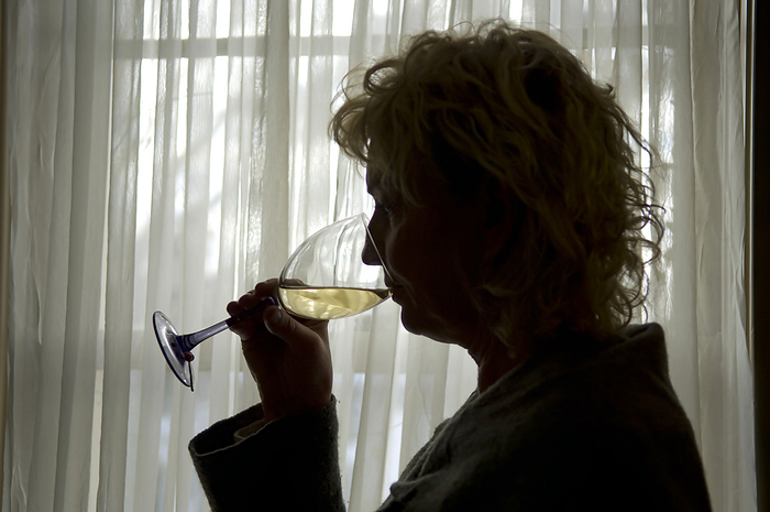 Woman drinking white wine alone in her home behind closed curtains; Lincoln, Nebraska, United States of America, by Joel Sartore Photography / Design Pics