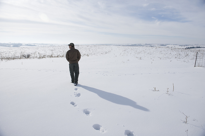 Man walking through a snowy pasture near Valparaiso in Nebraska, USA; Nebraska, United States of America, by Joel Sartore Photography / Design Pics